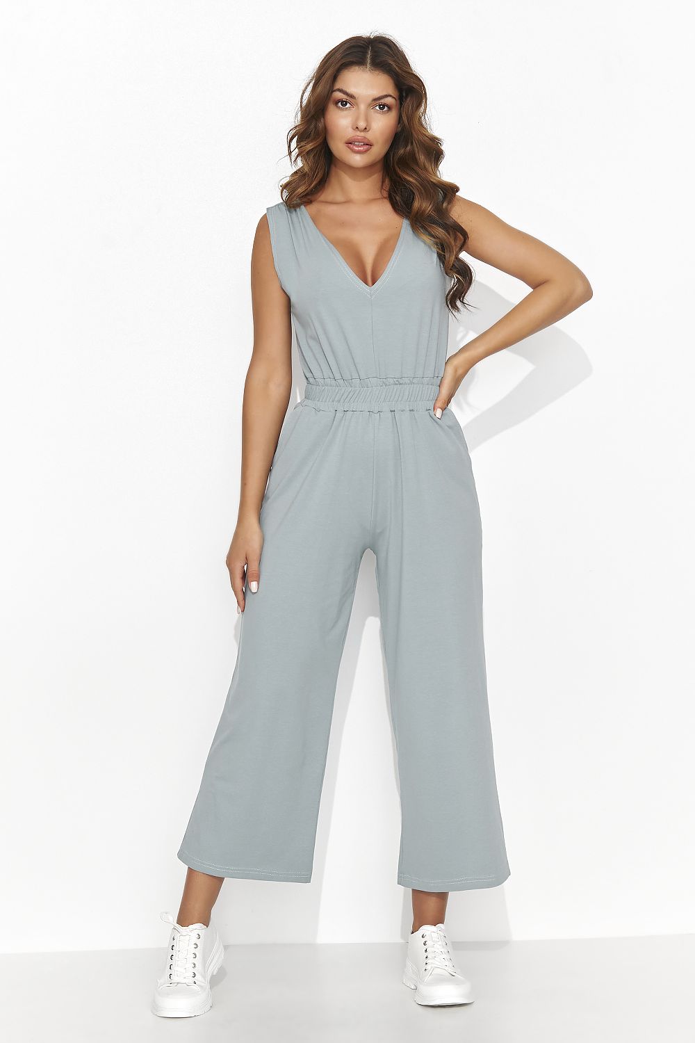 Vrouw draagt een gebreide Flare & Flow Knit Dream jumpsuit in mintgroen, combineert met rieten tas en zonnehoed op het strand